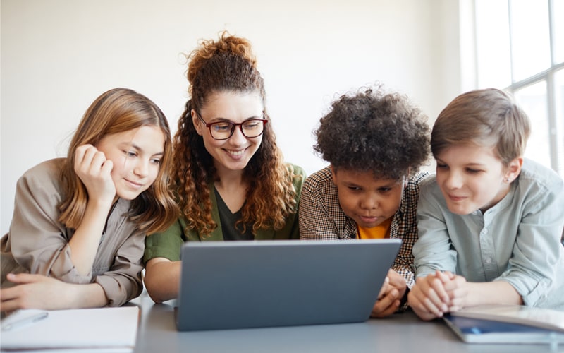 Children gathered, looking at the laptop.